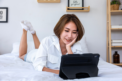 Young pretty girl working from home on her bed using digital tablet to access her business work for education study and online dating concept