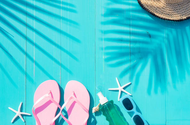 istock Composition viewed from above on turquoise blue planks with beach accessories, flip flops, sun cream, sunglasses, starfish and hat with shadows of palm leaves. Summer vacation concept. 2150522718