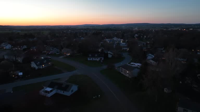 Drone flight over quiet district in american town at golden sunset. Road and street in suburbia of USA. Colorful lights at horizon in the evening. Dusk scene.