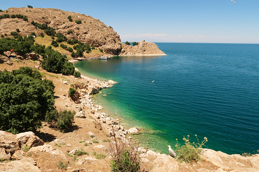 View onto the bay of Akdamar Island on Lake Van, Van Gölü with its little pier, jetty, intense blue, green, turquoise water and seagulls, Van, Turkey 2022