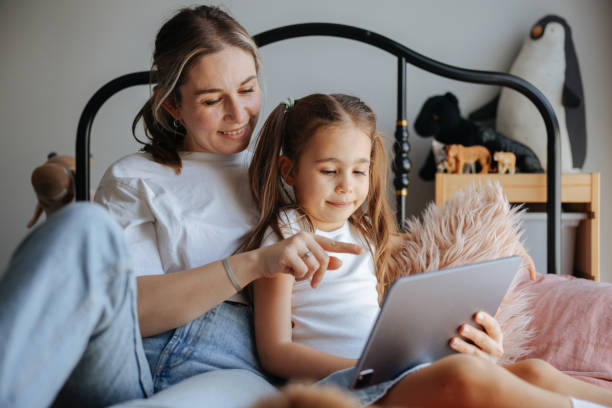 istock Mother and daughter watching their digital tablet together sitting on bed 2150529169