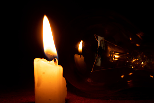 Incandescent lamp and candle in the dark at home, without light