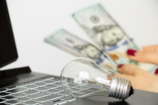 A girl counts dollars against the background of an incandescent light bulb and a laptop, light tariff