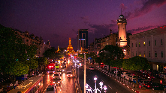 Streets of downtown Yangon Myanmar road to Sule Gold Pagoda sunset with traffic jam and modern city center. Buddhist sacred worship transport long exposure car light on street famous holy night town