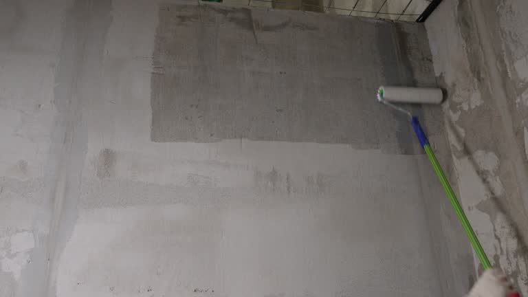 The process of applying primer to a wall using a roller. A worker primes walls in a new building. Roller brush with primer for plastering walls. Concept of building a house and renovating a house.