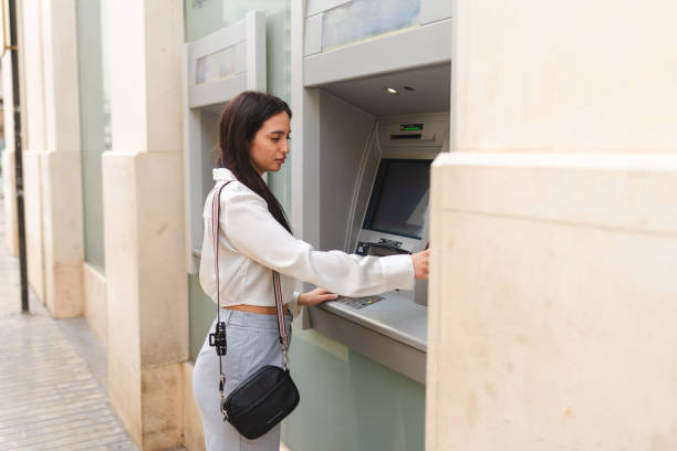 istock Beautiful young woman using the ATM 2150532050