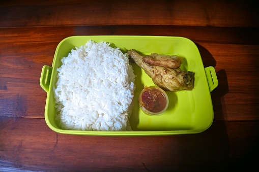 The green lunch box contains rice, fried chicken and chili sauce