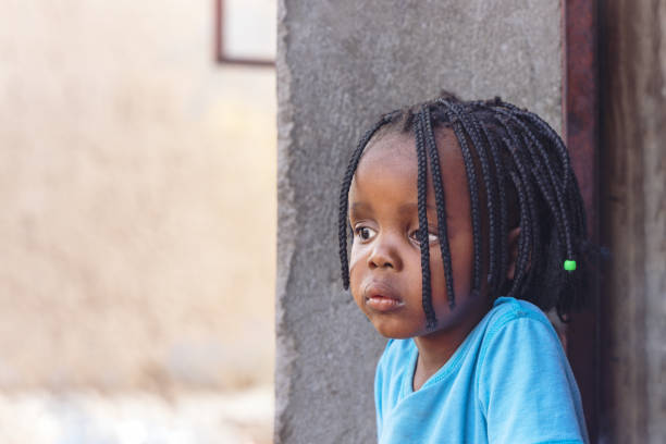 village single african small girl with braids standing in front of the door in the yard outdoors