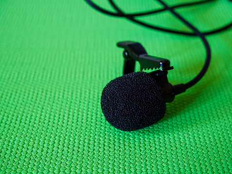 Audio Recording Gear. Wired lapel mic with clip against a green textured surface.