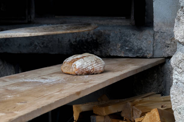 Male baker holding a fresh loaf of homemade sourdough bread.