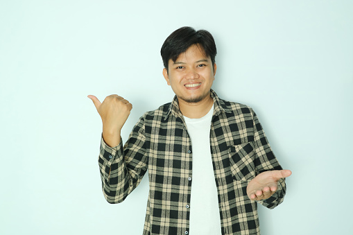 Young Asian man smiling and pointing to the right side with his thumb