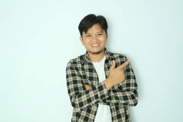 istock Young Asian man showing pointing finger to the left with smiling face 2150541411