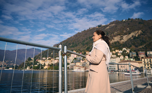Young multi ethnic pretty woman on waterfront, admiring the lake of Como in Italy. Beautiful Alpine mountains on the background. People. Travel destinations. Tourism. People. Lifestyle