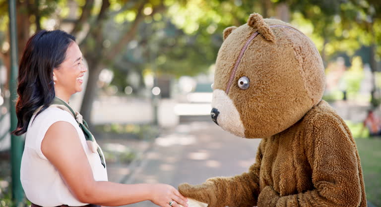 Bear, handshake and woman with costumer, greet and outdoor with hello and agreement with feedback. Halloween,  costume and girl in a park, shaking hands and conversation with communication and review