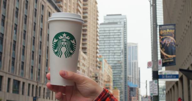 Toronto, Canada - May 6, 2023: Hand holds Starbucks cup, iconic urban backdrop. City hustle flows as Starbucks offers familiar comfort. Emblematic coffee moment in metropolitan life. Starbucks concept
