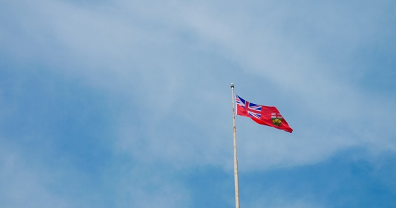 Fluttering British colony flag, vivid against blue sky, symbolizes historic pride, enduring legacy. National emblem waves, reflecting past sovereignties, colonial history. Not official Flag of Canada.