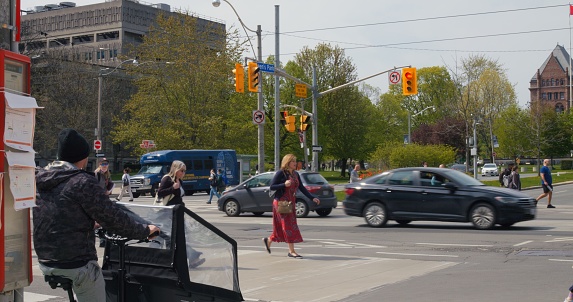 Toronto, Canada - May 6, 2023: Urban hustle captured in busy intersection, modern tram glides by. City life rhythm with pedestrians, cyclist in view. Urban vibe, diverse crowd, dynamic street scene