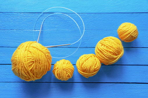 Hobby and knitting concept. Yellow balls of wool and knitting needles on blue rustic table