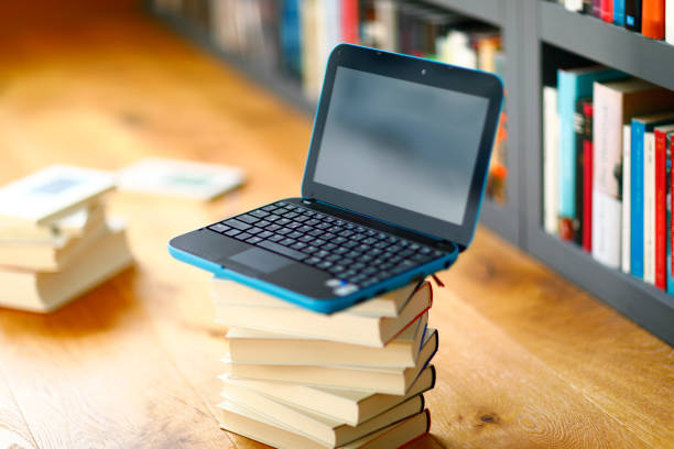 Laptop on a stack of hardcover books in front of a bookshelf