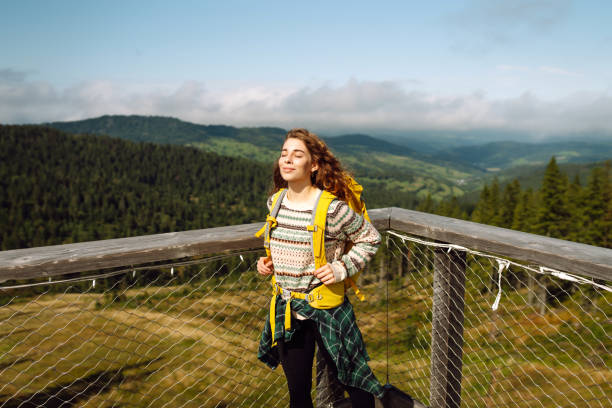 Young woman on wooden bridge with backpack among treetops. Concept of freedom, travel, lifestyle.