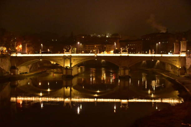 A suggestive and idyllic twilight view of the Tiber riverbank, in the historic heart of Rome. On the left, the Vittorio Emanuele II bridge, while on the horizon stands the imposing silhouette of the dome of St. Peter's Basilica. In 1980 the historic center of Rome was declared a World Heritage Site by Unesco. Super wide angle image in 16:9 and high definition format.