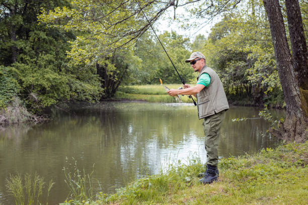 istock Angler standing on a riverbank and successfully catching a fish 2150575325