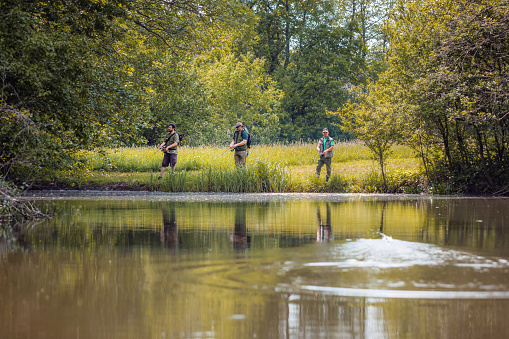 Three anglers enjoying fishing surrounded by the lush green nature of the river shore. Outdoor hobby and activity concept.