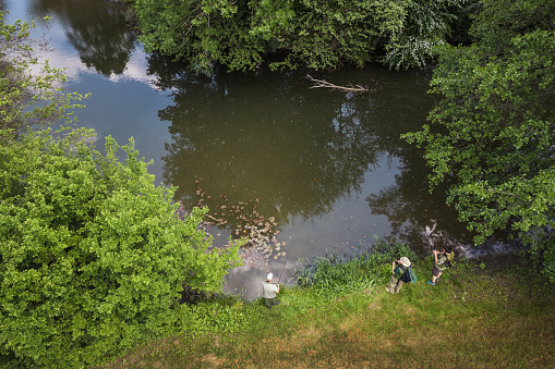 Rear view of three sports fishermen enjoying fishing in tranquil river surroundings, aerial shot. Vacation, hobby, and leisure activity concepts.