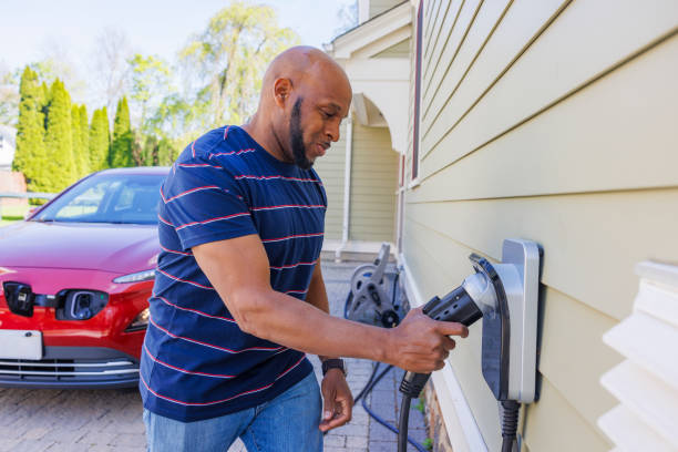 istock Utilizing renewable energy: a happy African American man is seen plugging a charging cable into an electric vehicle charger installed at his suburban home in Madison, New Jersey 2150578372