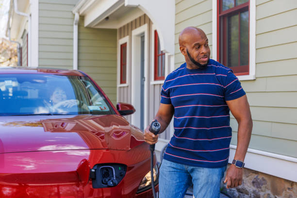 istock Responsible commuting with modern technology. Smiling man with power cable is charging the EV at home yard in Madison, NJ 2150578379