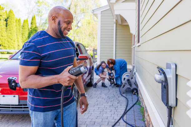 istock Eco-conscious vacation: African-American man using EV charger while his family playing with dog in background 2150578394