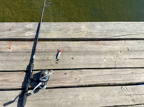 Fishing tackle - spinning rod with box of lures and equipment on a wooden background near water