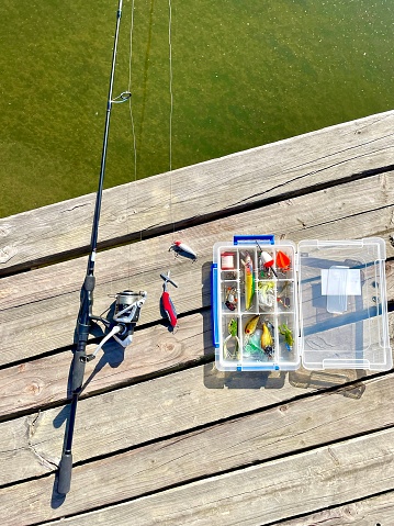 Fishing tackle - spinning rod with box of lures and equipment on a wooden background near water