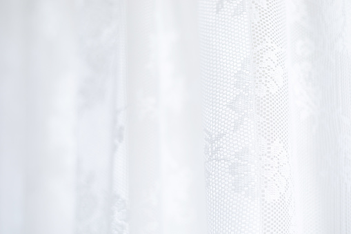 Abstract light background of white lace fabric is showcased in soft lighting.