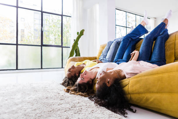 istock Three happy female friends lying upside down on sofa - Young multiracial women having fun while laughing together at home - Focus in caucasian woman - Copy space for text 2150587274