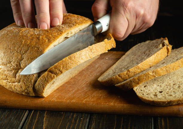 istock Close-up of a chef hands with a knife cutting rye bread on a kitchen cutting board. Bread on the kitchen table or healthy eating and traditional bakery products concept 2150588845