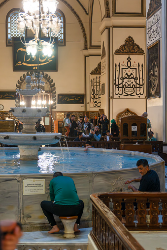 Bursa, Turkey - April 13, 2024: View of the inside of the Grand Mosque and Muslims performing ablution in the fountain