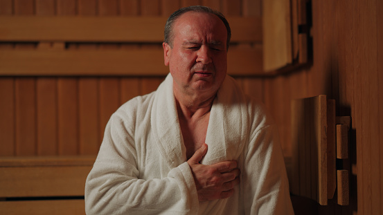 A senior man is feeling heart and chest pain in a sauna.