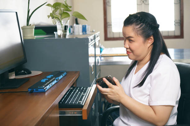 Woman with blindness disability using smart phone with voice accessibility for persons with disabilities in workplace with computer and refreshable braille display a technology assistive device for persons with visual impairment