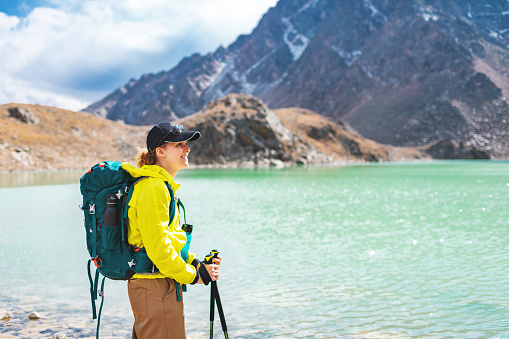 Mid adult woman trekking near mountain lake, standing and looking at view