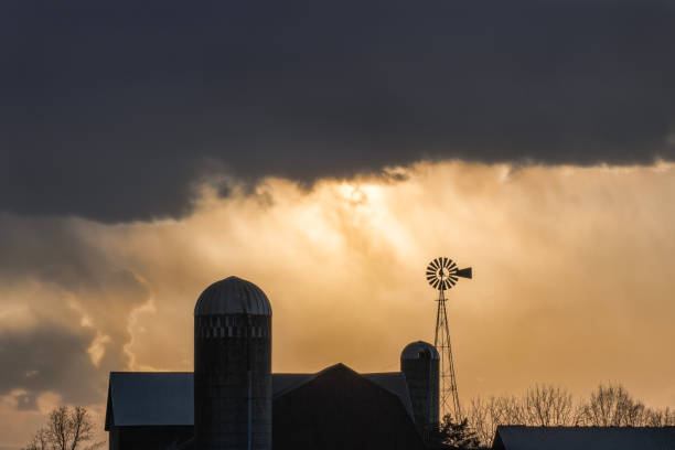 An old barn stands in a rural field under imposing, incoming storm clouds.