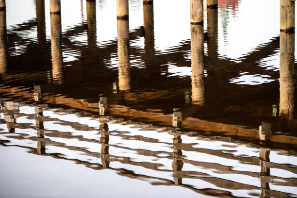 Wooden bridge over the river with reflection in the water surface. Many wooden bridges were pearls of wooden architecture throughout Europe. Unprotected wood was subject to natural degradation and decay processes. The construction elements were most often made of oak and hewn wood, over time they were replaced with resin wood, e.g. pine, fir, which better resisted the destructive effects of water.