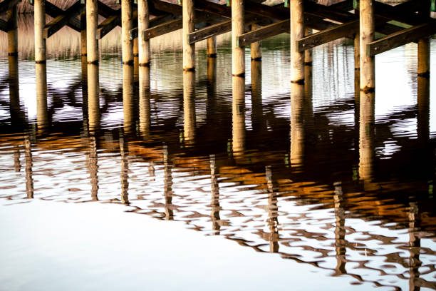 Wooden bridge over the river with reflection in the water surface. Many wooden bridges were pearls of wooden architecture throughout Europe. Unprotected wood was subject to natural degradation and decay processes. The construction elements were most often made of oak and hewn wood, over time they were replaced with resin wood, e.g. pine, fir, which better resisted the destructive effects of water.
