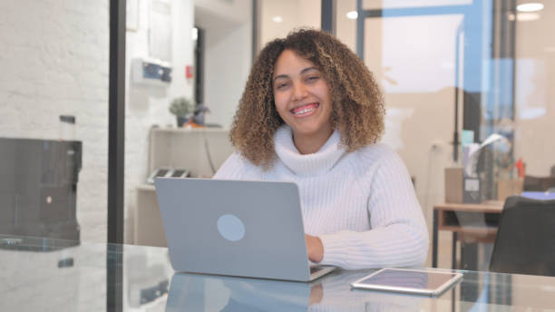 istock African Woman Smiling at Camera while Working on Laptop in Office 2150607491