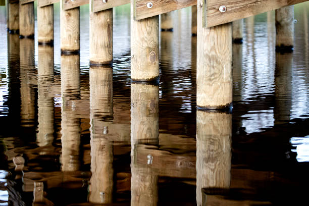 Wooden bridge over the river with reflection in the water surface. Many wooden bridges were pearls of wooden architecture throughout Europe. Unprotected wood was subject to natural degradation and decay processes. The construction elements were most often made of oak and hewn wood, over time they were replaced with resin wood, e.g. pine, fir, which better resisted the destructive effects of water.