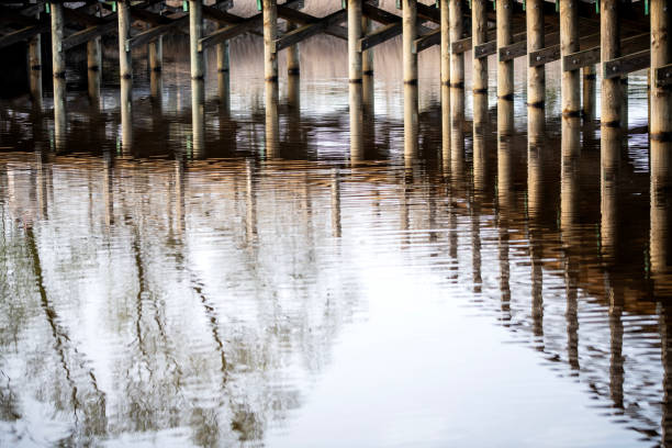 Wooden bridge over the river with reflection in the water surface. Many wooden bridges were pearls of wooden architecture throughout Europe. Unprotected wood was subject to natural degradation and decay processes. The construction elements were most often made of oak and hewn wood, over time they were replaced with resin wood, e.g. pine, fir, which better resisted the destructive effects of water.