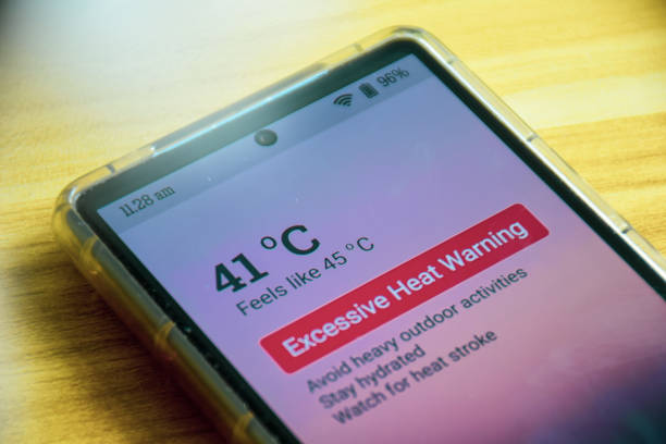 Excessive heat warning alert on mobile phone. Selective focus. Extreme weather, El Nino condition. Wooden background.
