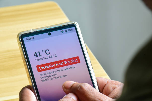 istock Man mobile phone displaying Excessive heat warning alert. Selective focus, man hand holding. Extreme weather, El Nino condition. Wooden background. 2150610588