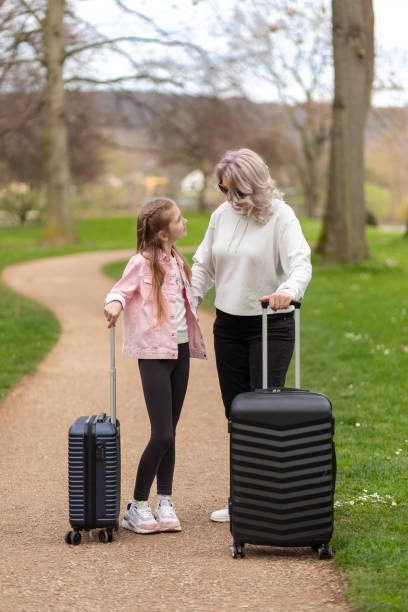 Woman and girl having a conversation while walking with suitcases in a park