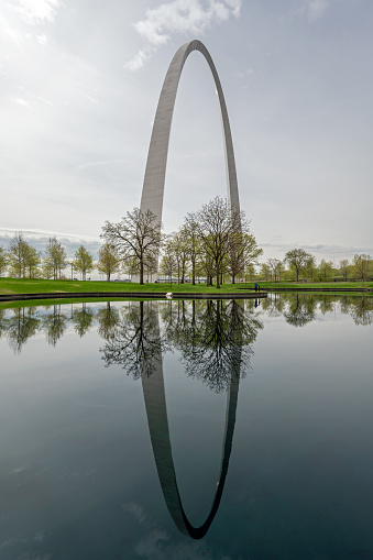 Saint Louis, Missouri - April 9. 2024 - Gateway Arch reflected in reflecting pool in Gateway Arch National Park under dramatic spring cloudscape.